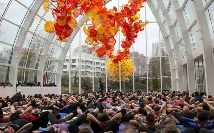 The art of Dave Chihuly hangs above yogis who are using the space as a Seattle event venue